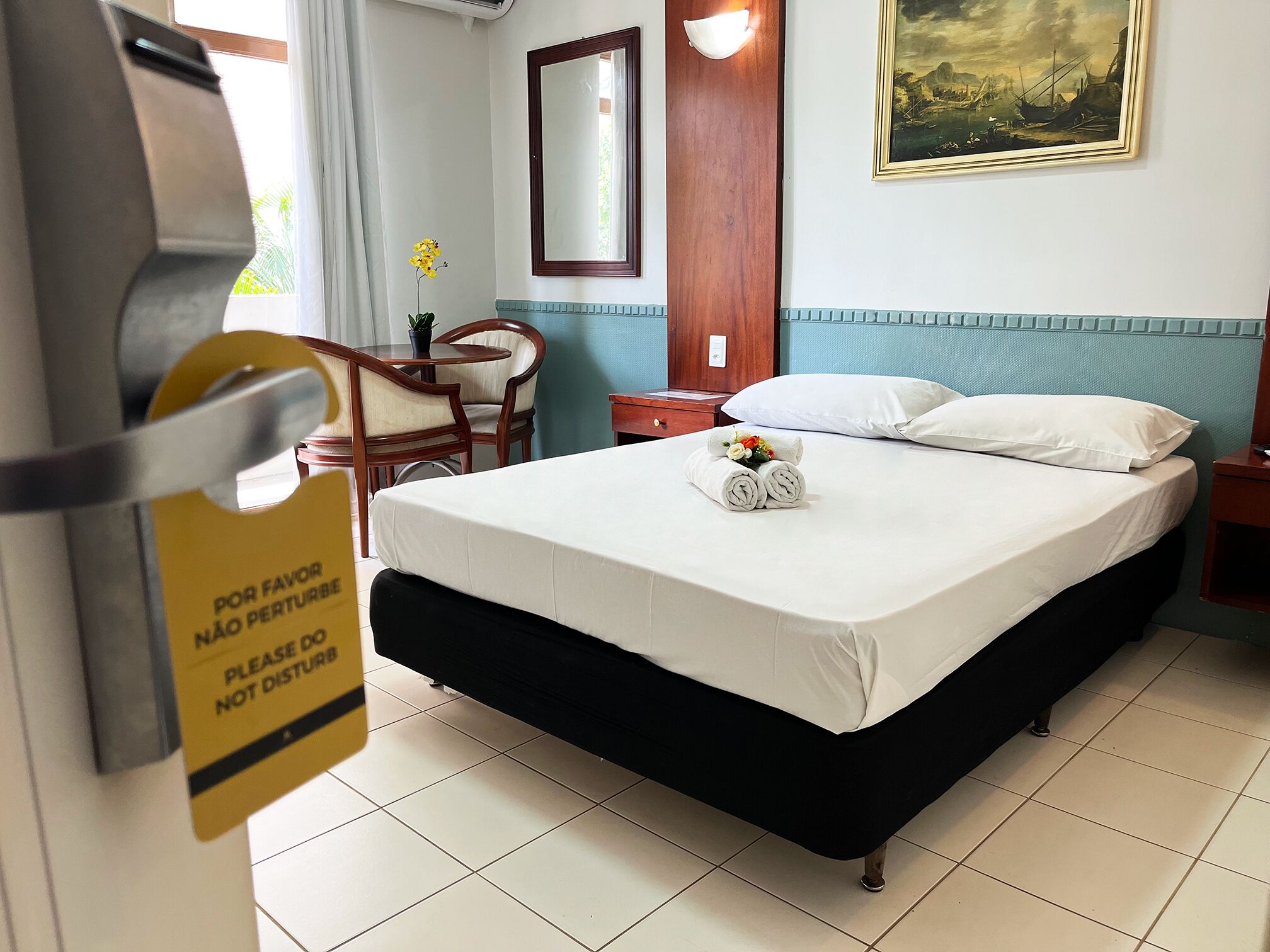 Una camera d'albergo con un letto, una scrivania, una sedia, un comodino, uno specchio e un quadro appeso al muro.