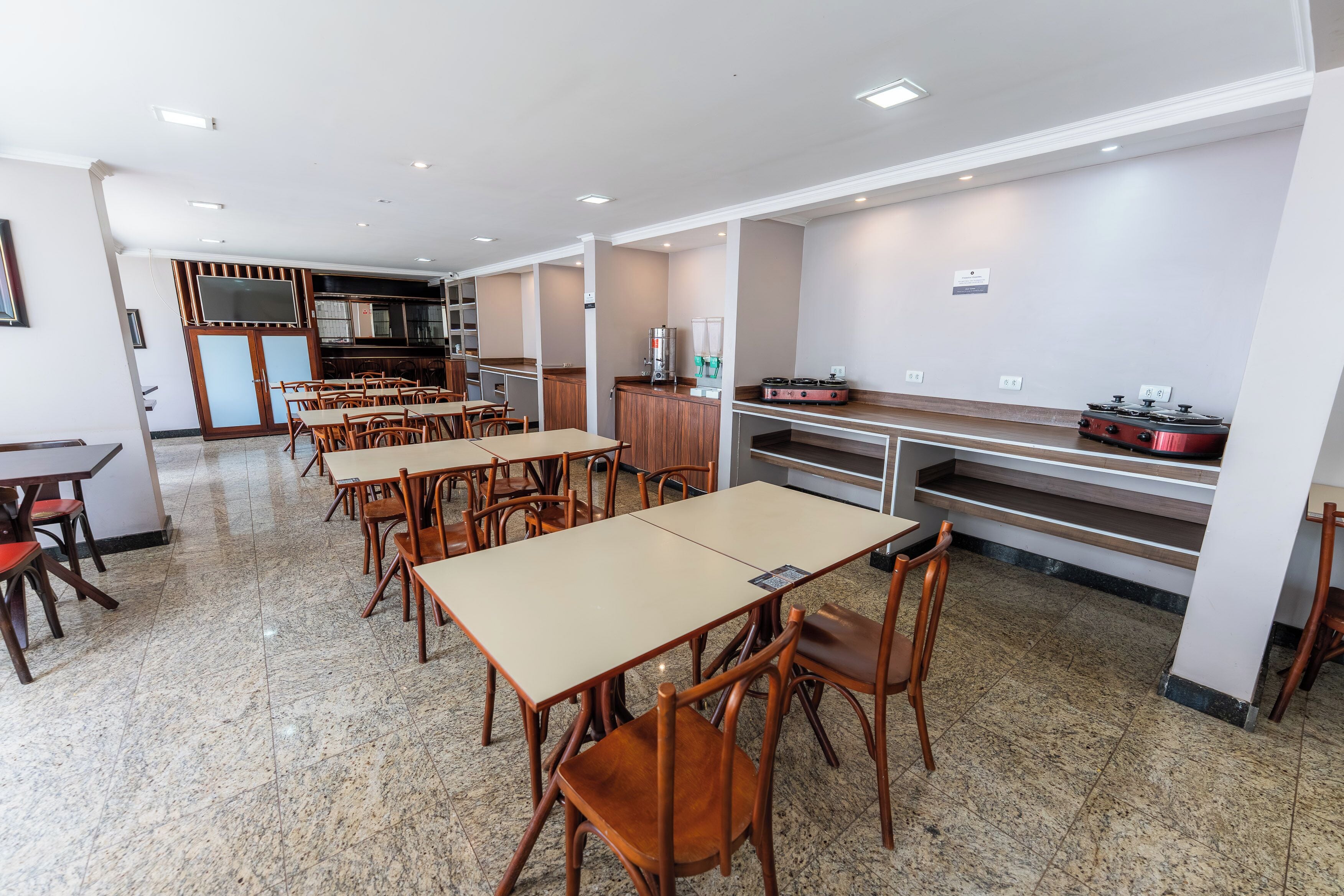 A spacious dining area with multiple tables and chairs, a kitchen area with appliances, and a counter with a coffee machine.