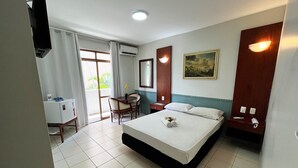 A hotel room with a bed, a desk, a chair, a small table with a flower, and a painting on the wall. - Hotel Alvorada by Bsb Inn (Taguatinga)