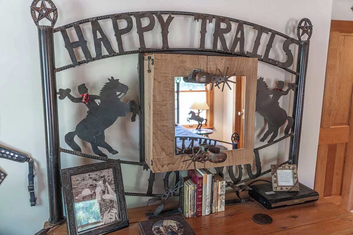 A rustic metal sign with 'HAPPY TRAILS' and silhouettes of horses.