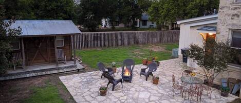 Un patio de piedra con mobiliario exterior, una fogata y un pequeño jardín.