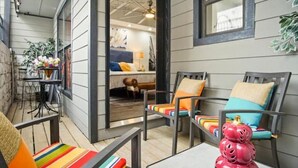Un espace extérieur accueillant avec une table et des chaises, une petite table décorée de fleurs et une vue sur une pièce où l’on aperçoit un lit et une fenêtre.
