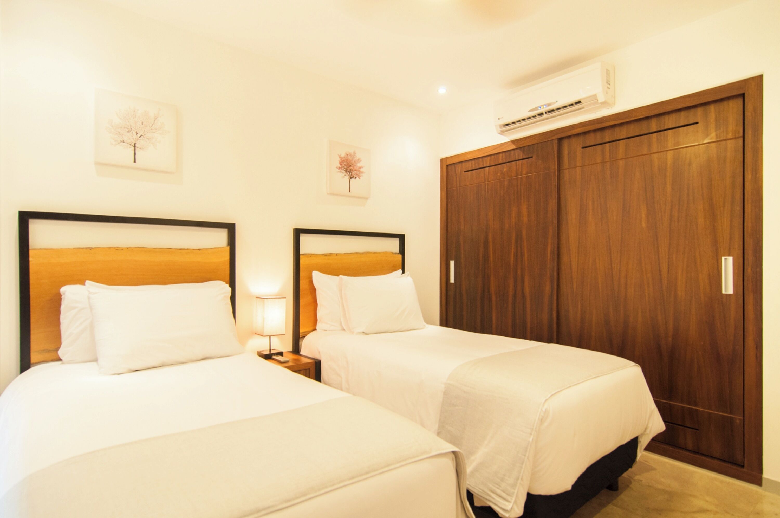 A hotel room with two beds, a wooden wardrobe, and wall-mounted air conditioning.