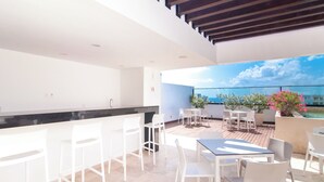 A modern outdoor dining area with white furniture and a view of the sea. - Kuxtal 3 Bedroom Downtown Apartment  (Playa del Carmen)