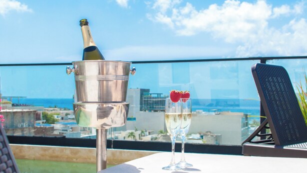 A rooftop terrace with a champagne bottle in a bucket, two champagne glasses, and a view of the city and sea. - Kuxtal 3 Bedroom Downtown Apartment  (Playa del Carmen)