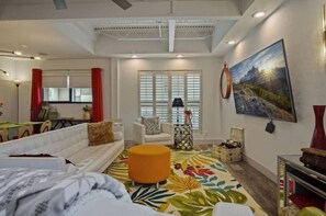 A modern living room with a sofa, ottoman, and a large painting on the wall.