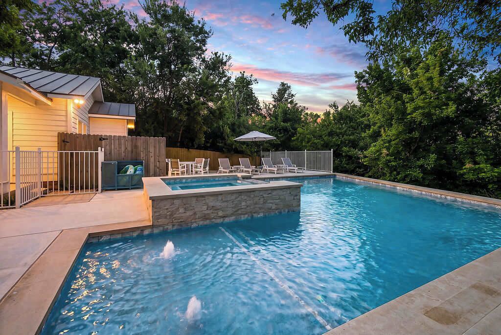 Ein Pool mit Wandverkleidung aus Stein, umgeben von einem Holenzaun und Liegestühlen.