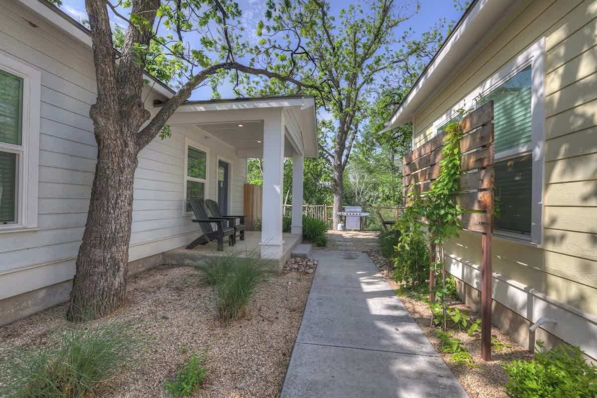 A covered patio area with outdoor seating, a tree, and a pathway leading to a house.