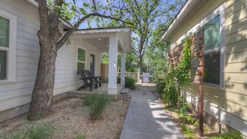 A covered patio area with outdoor seating, a tree, and a pathway leading to a house.