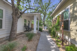A covered patio area with outdoor seating, a tree, and a pathway leading to a house. - The Grove E With Hot Tub & King Bed - 2 Blks to Main (Fredericksburg)