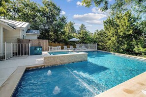 A swimming pool with a stone accent wall, surrounded by a wooden fence and lounge chairs.