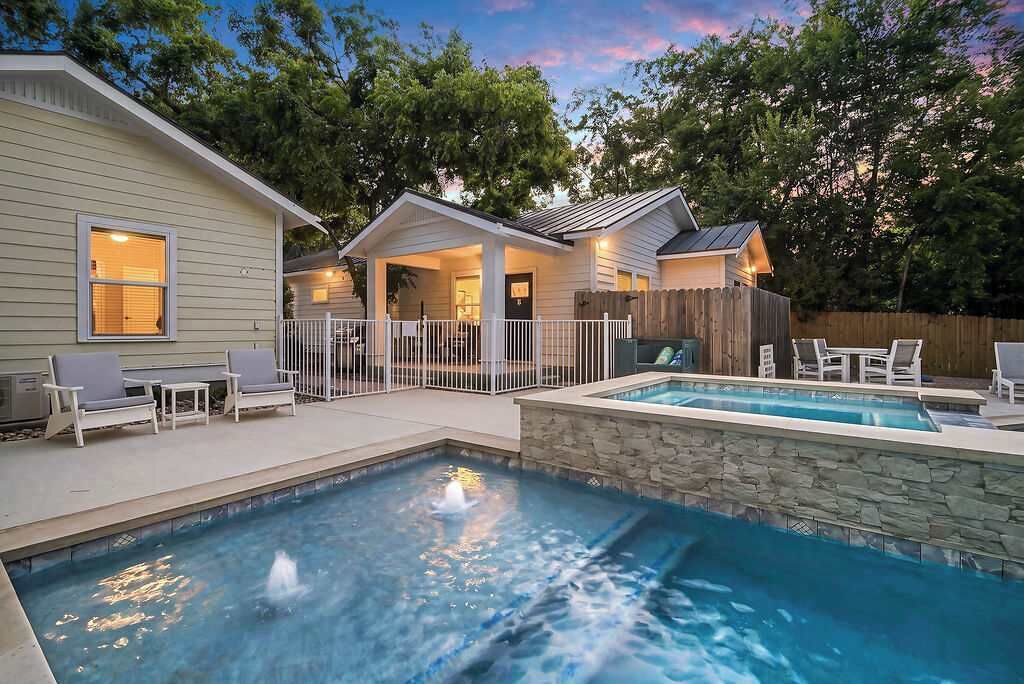 A residential property with a swimming pool, outdoor seating, and a covered patio area.