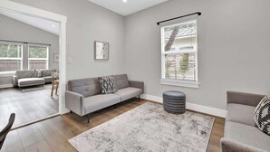 A modern living room with a grey sofa, a grey ottoman, and a patterned rug.