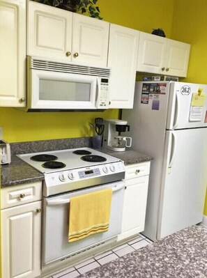 Une cuisine avec des meubles blancs, un four à micro-ondes, une cuisinière et un réfrigérateur.