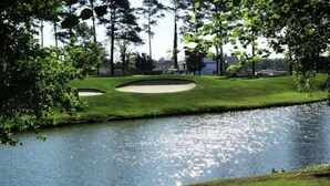 A golf course with a pond, surrounded by trees and buildings in the background. - Gorgeous 1st Floor Condo at Arrowhead Country Club
 (Myrtle Beach)