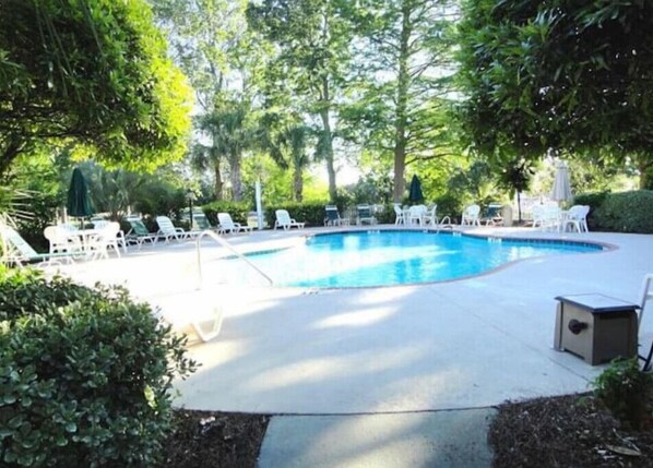 Relax by the serene pool surrounded by lush greenery and trees, with lounge chairs and a clear blue water surface.
