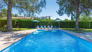 A rectangular swimming pool with clear blue water, surrounded by a stone deck. There are several lounge chairs aligned along the poolside, and two umbrellas providing shade. - Villa Camarasa by Balearic Villas (Pollensa)