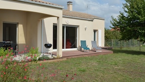 Ein Haus mit Terrasse, Grill und überdachter Sitzgelegenheit im Freien.