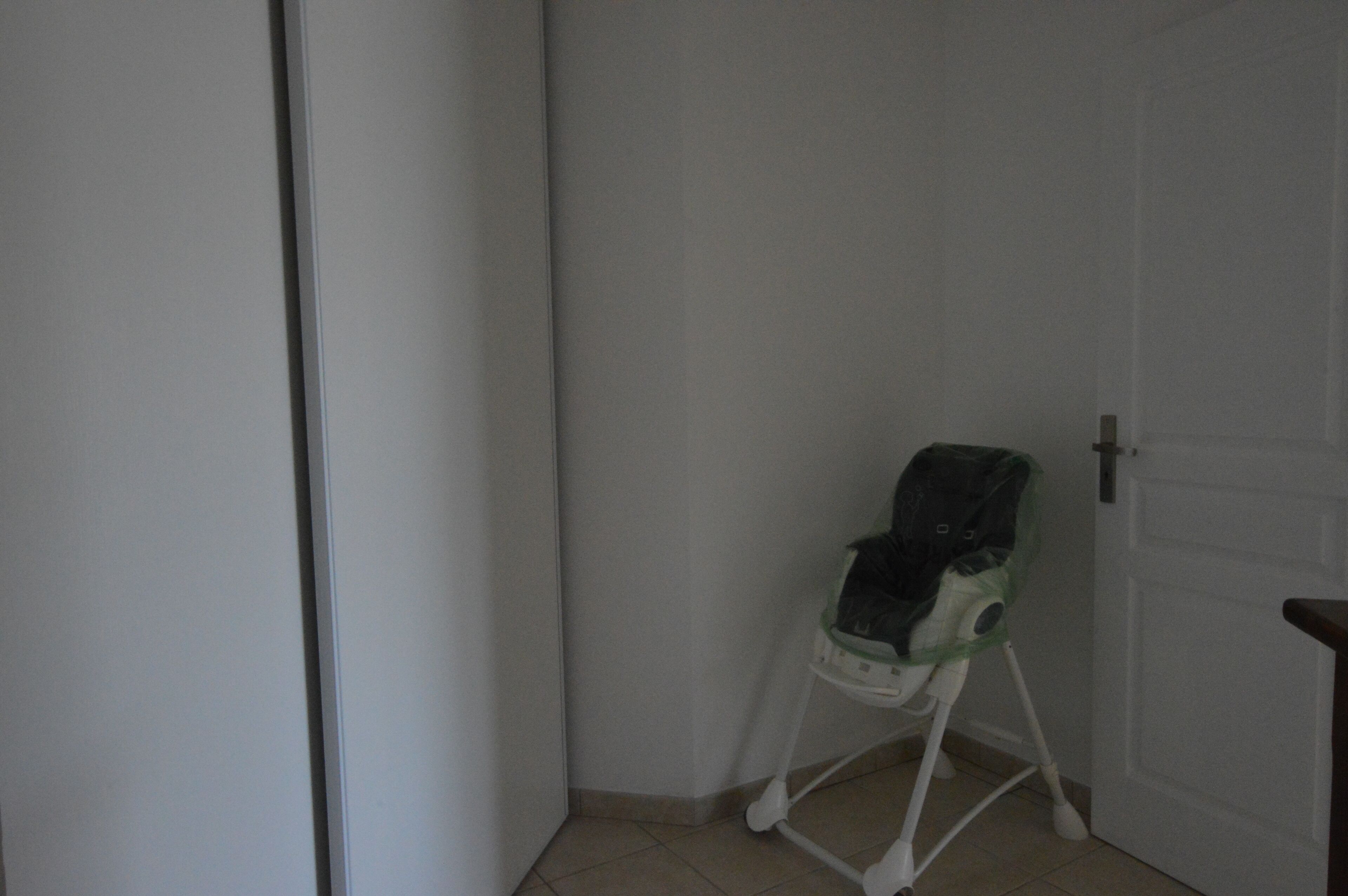 Esquina de una habitación con una puerta blanca, una pared blanca y un andador para bebé blanco.