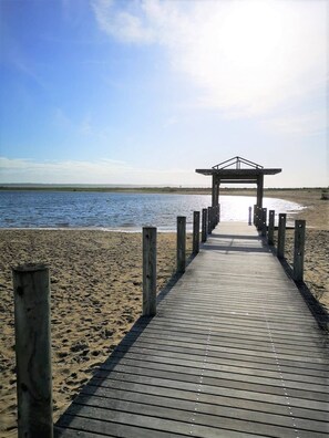 Un paseo marítimo de madera que conduce a una playa, con una estructura de madera al final.