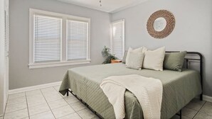 A bedroom with a bed, white blinds, a ceiling fan, and a wall-mounted air conditioner.