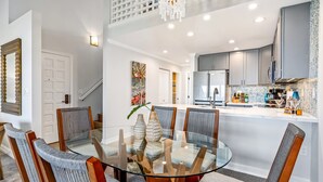 A modern kitchen with grey cabinets, a central island, and a dining area with a glass table and chairs. - Luxurious & Spacious Ocean Vistas (Kihei)