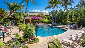 A pool area with lounge chairs, palm trees, and a building in the background. - Luxurious & Spacious Ocean Vistas (Kihei)
