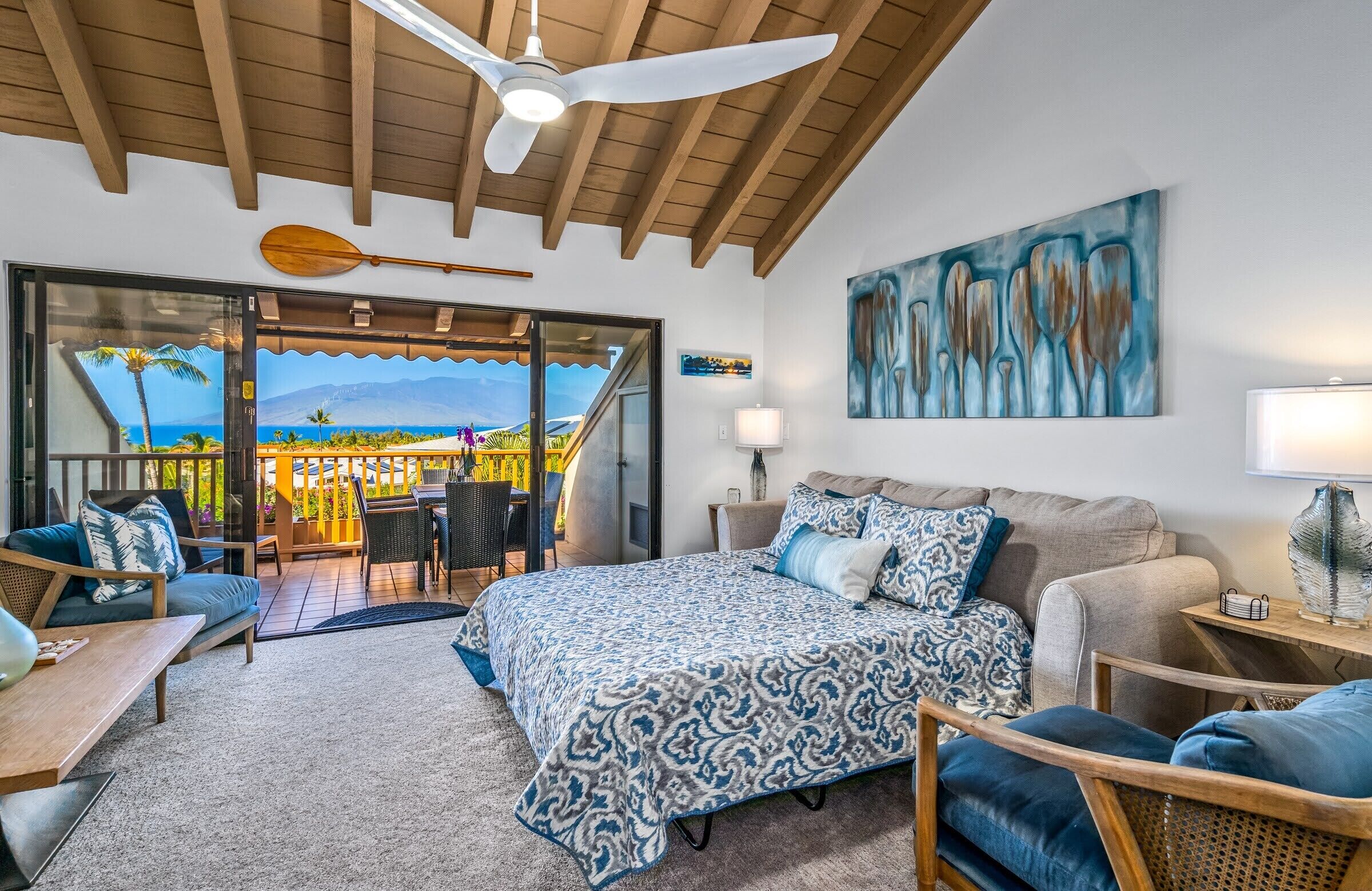 Een ruime slaapkamer met een groot bed, een plafondventilator en uitzicht op de oceaan door een schuifdeur.