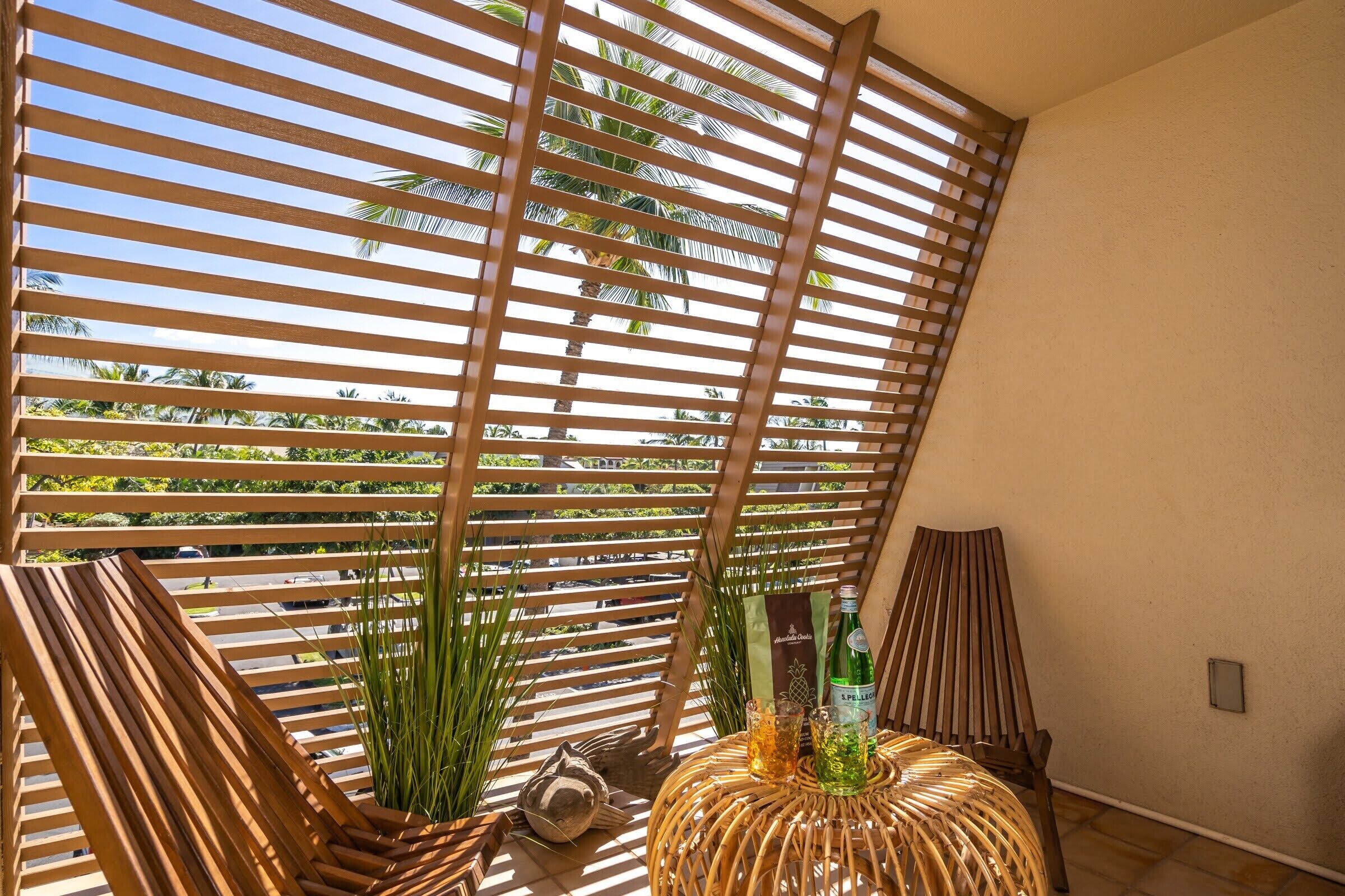 A room with a slatted wooden partition, a wicker table with a bottle and glass, and a chair.