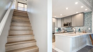 A modern kitchen with a central island, built-in appliances, and a staircase leading to an upper level. - Luxurious & Spacious Ocean Vistas (Kihei)