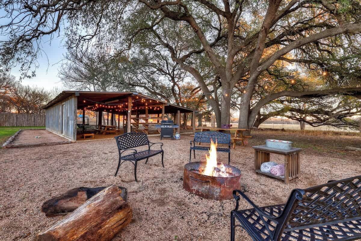 An outdoor patio area with a fire pit, metal chairs, and a covered seating area.