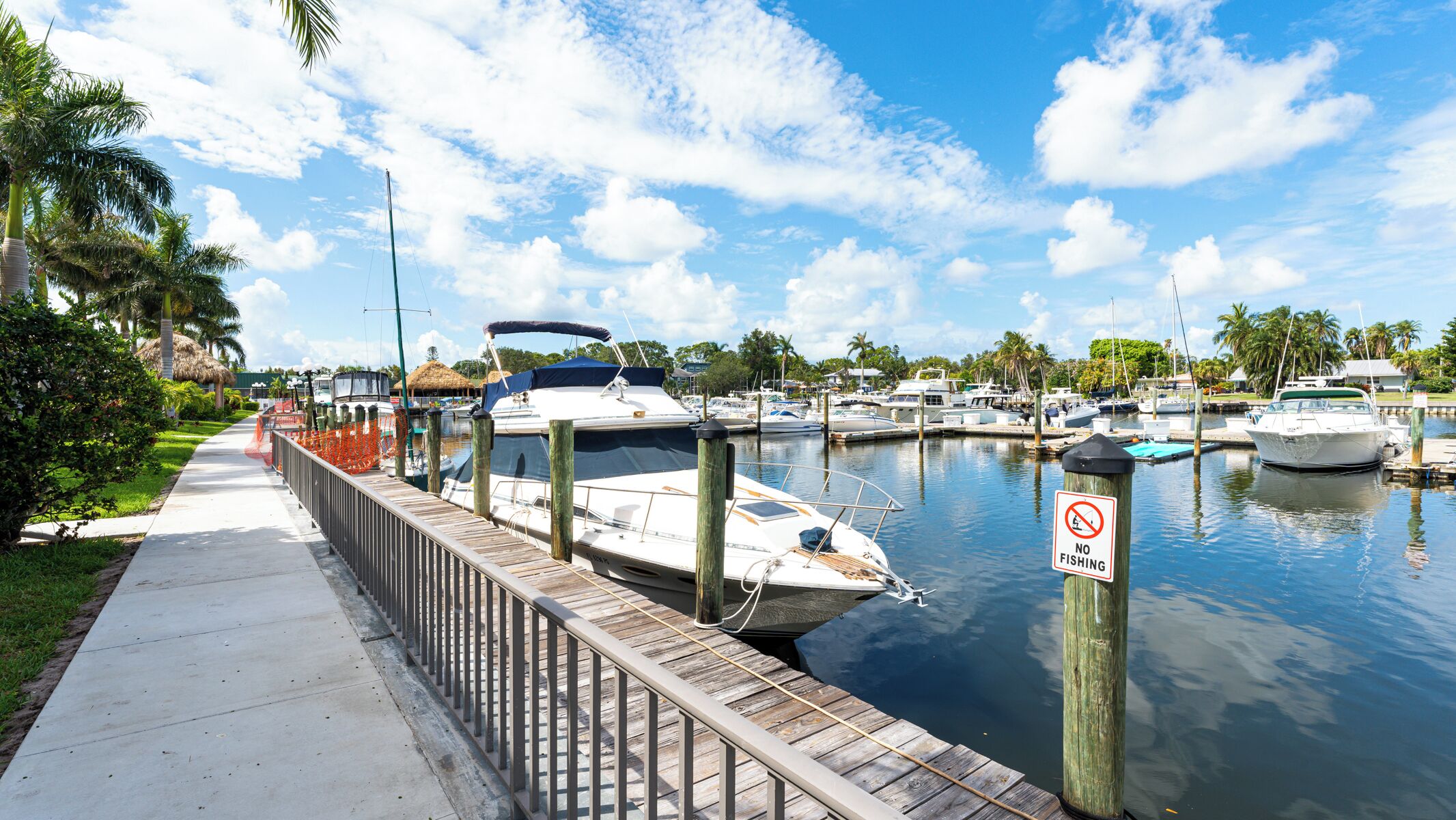 A marina with boats docked, a no fishing sign, and a wooden walkway alongside the water.
