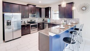 Una cocina moderna con armarios oscuros, electrodomésticos de acero inoxidable, encimera de granito y taburetes de bar.