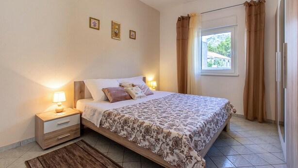 Une chambre à coucher avec un lit, des tables de chevet, une fenêtre avec des rideaux et une vue sur l’extérieur.