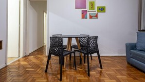 Ein Essbereich mit Holzdielenmuster-Boden, einem schwarzen Metalltisch und Stühlen. Vier gerahmte Kunstwerke sind an der Wand zu sehen.