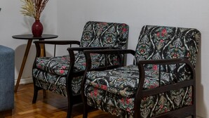 Ein Zimmer mit Holzboden, zwei gemusterte Sessel, einem kleinen runden Tisch mit einer Vase und einem großen Spiegel an der Wand.