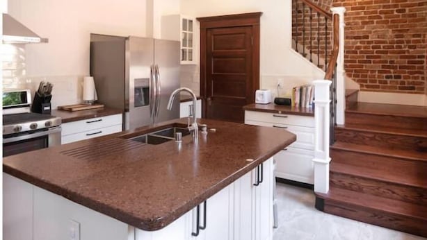 A modern kitchen with a central island, stainless steel appliances, and a brick accent wall. - Casa de Los Artistas (Albuquerque)