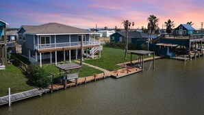 A waterfront property with a large house featuring a covered porch and a dock extending into the water.