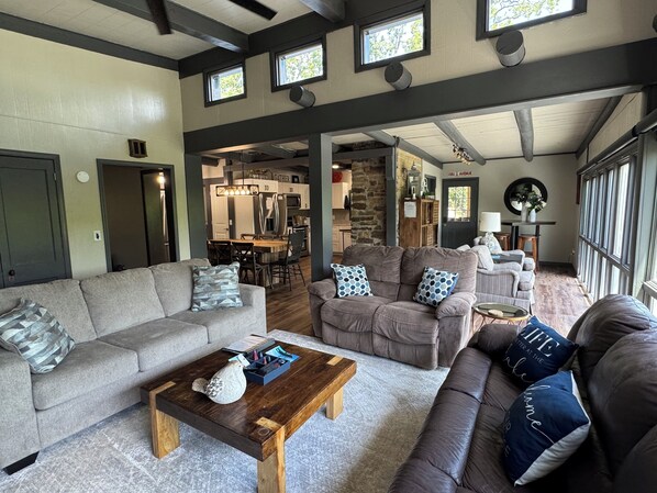 Ein geräumiges Wohnzimmer mit einer großen Couch, einem Couchtisch und einem Essbereich, wobei im Hintergrund eine Küche zu sehen ist.