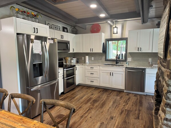 Una cocina moderna con armarios blancos, electrodomésticos de acero inoxidable, una mesa de comedor de madera y una pared decorativa de piedra.