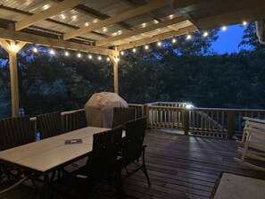 A covered outdoor patio with a table and chairs, string lights, and a grill.