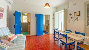 A room with a red tiled floor, a blue sofa, a dining table with blue chairs, and a kitchen area visible through an open door. - Pet friendly home in Trani with WiFi (Trani)