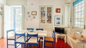A dining area with a white table and blue chairs, a television on a small table, and a cabinet with glass doors containing dishes and a framed picture. - Pet friendly home in Trani with WiFi (Trani)