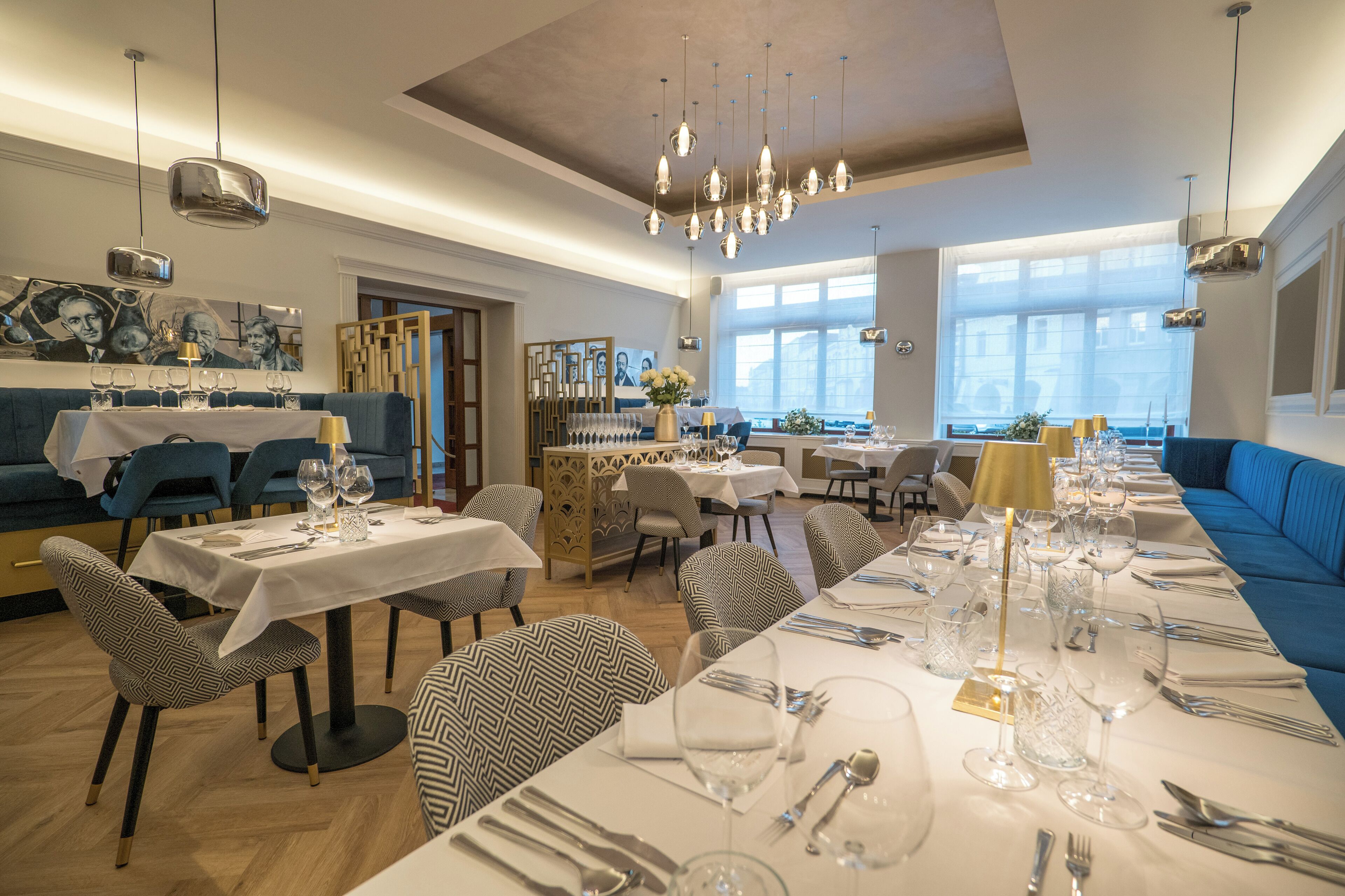 A restaurant with multiple tables set for dining, a blue sofa, and a chandelier.