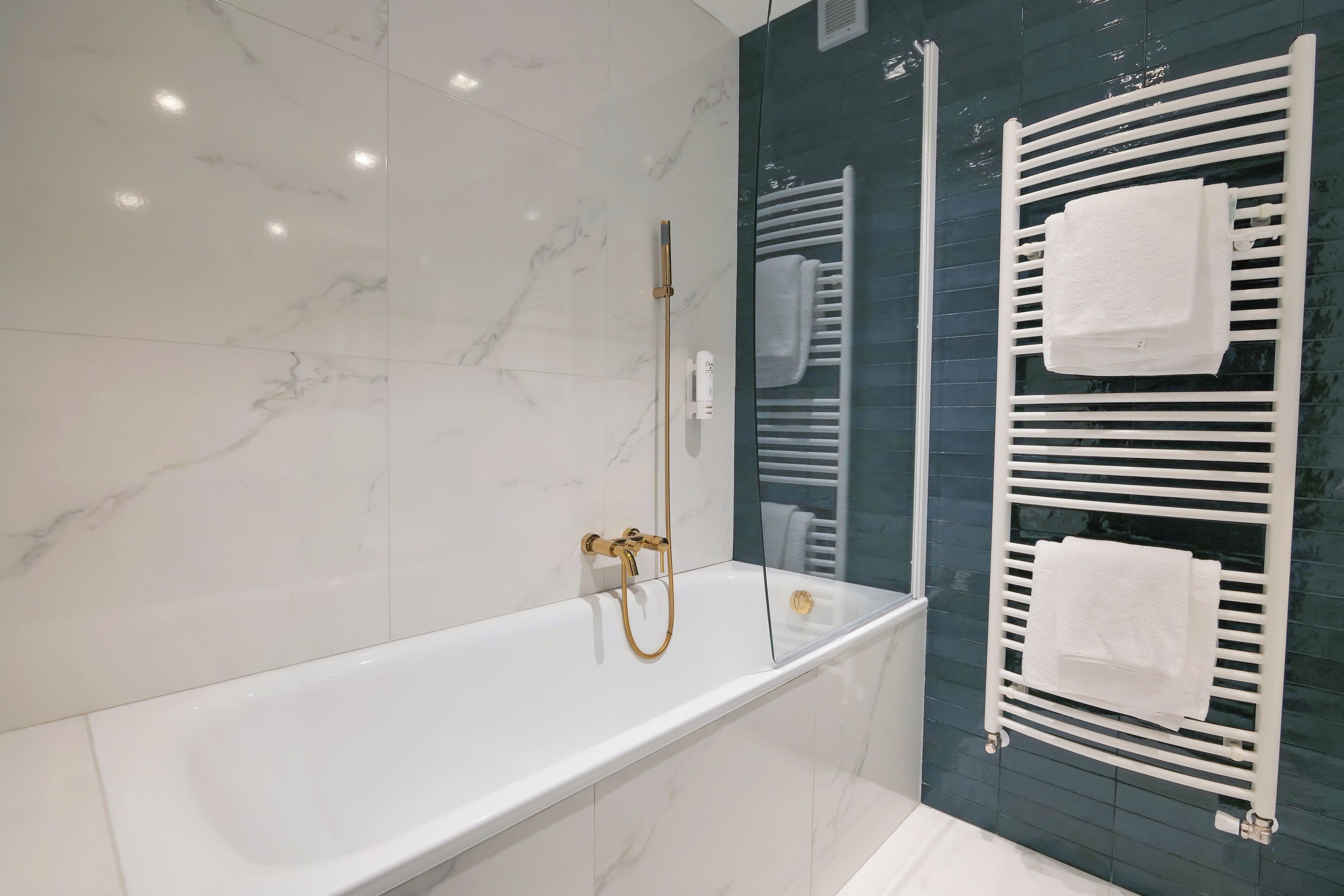 Un baño moderno con una bañera blanca, un cabezal de ducha dorado y un perchero con toallas.