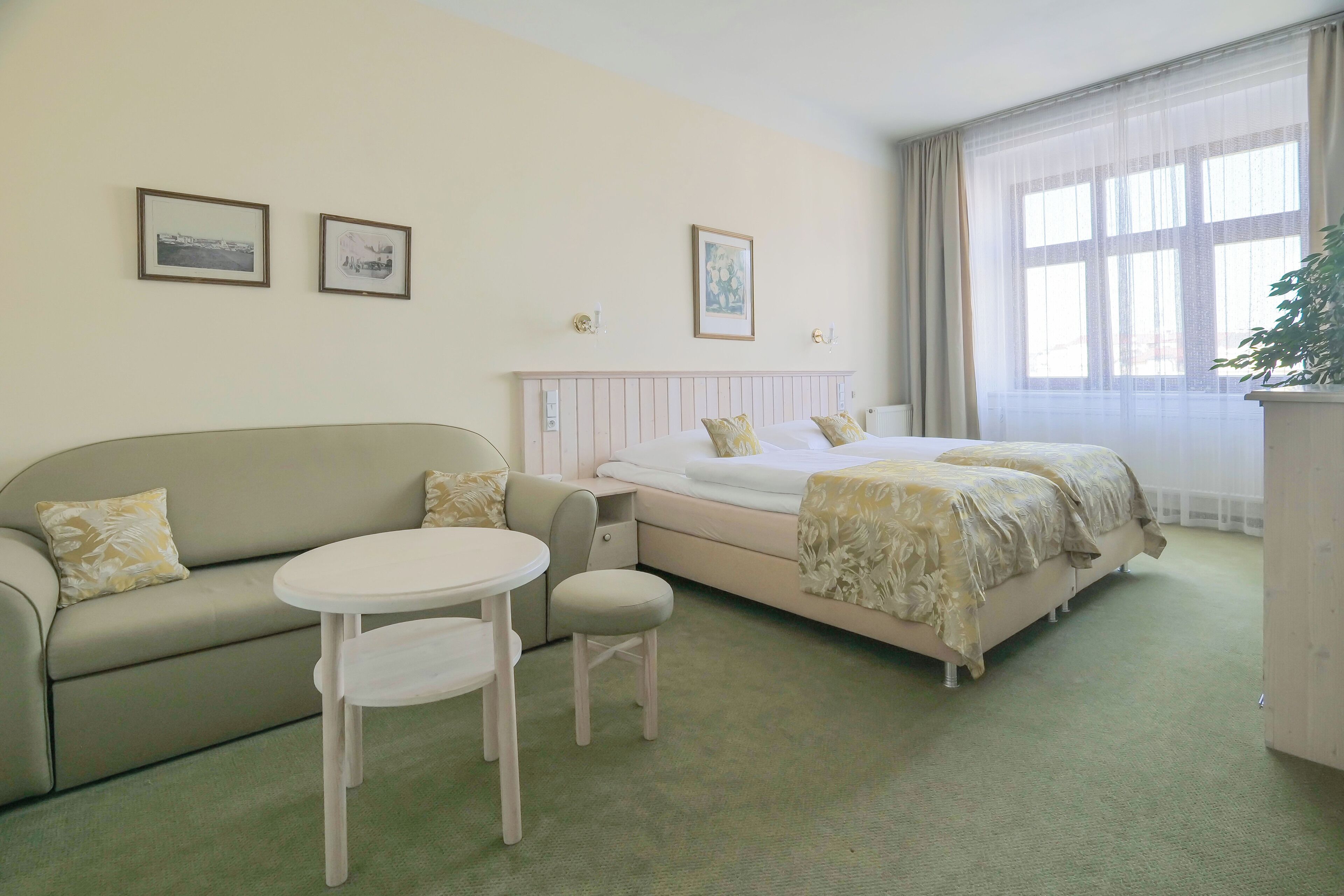 Une chambre d’hôtel avec un lit, un canapé, une petite table et une chaise. Il y a trois tableaux encadrés accrochés au mur.