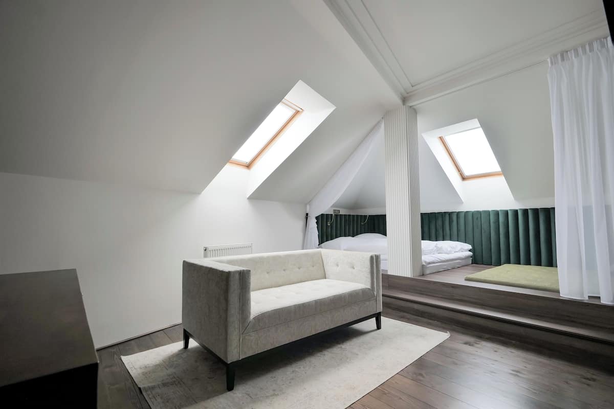 A modern loft bedroom with a high ceiling, skylights, a bed with green curtains, a sofa, and a small rug.