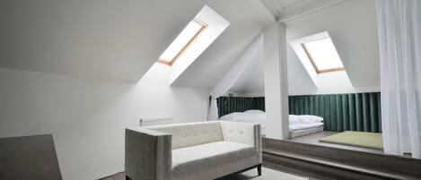 Un dormitorio tipo loft moderno con techo alto, tragaluces, cama con cortinas verdes, un sofá y una alfombra pequeña.