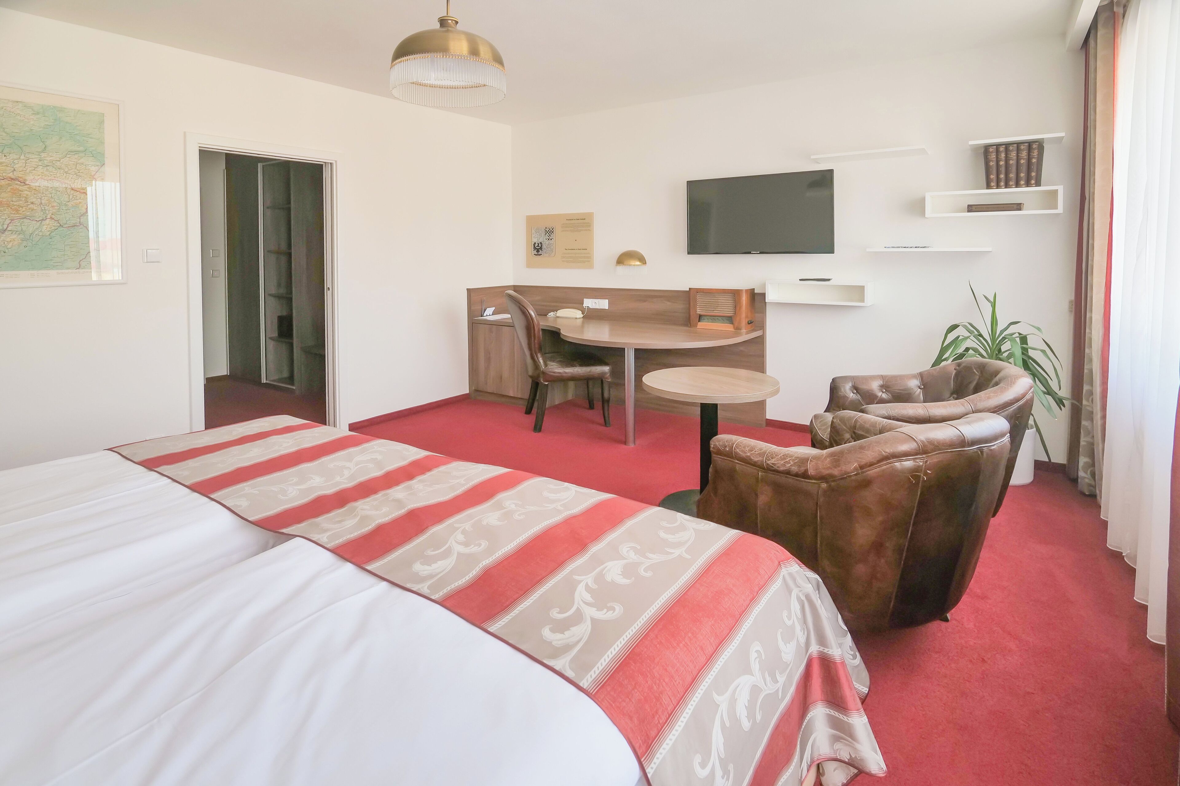 Een hotelkamer met een groot bed, een bureau met stoel, een televisie en een plant.
