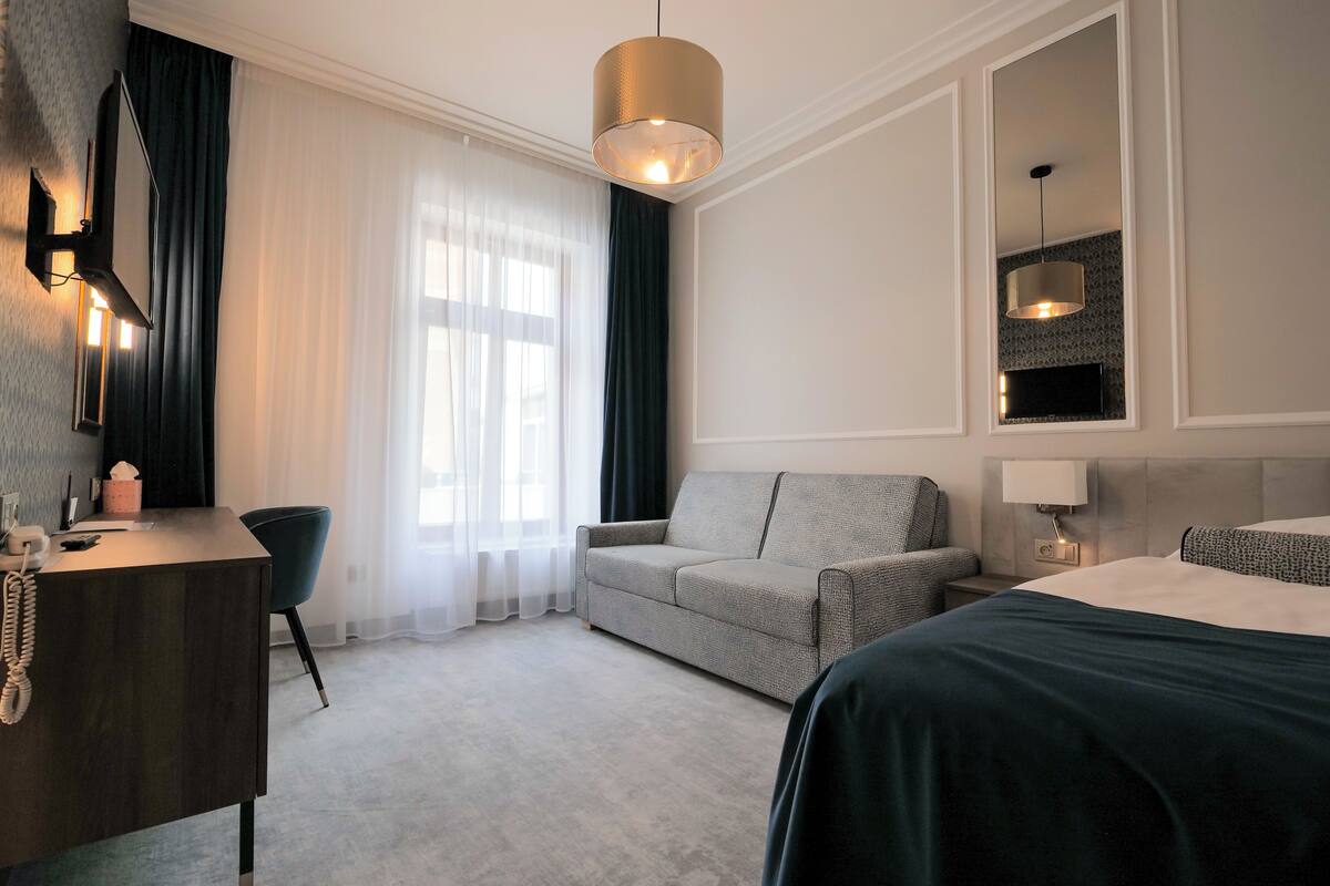 A hotel room with a bed, a desk, a chair, a sofa, and a TV mounted on the wall.